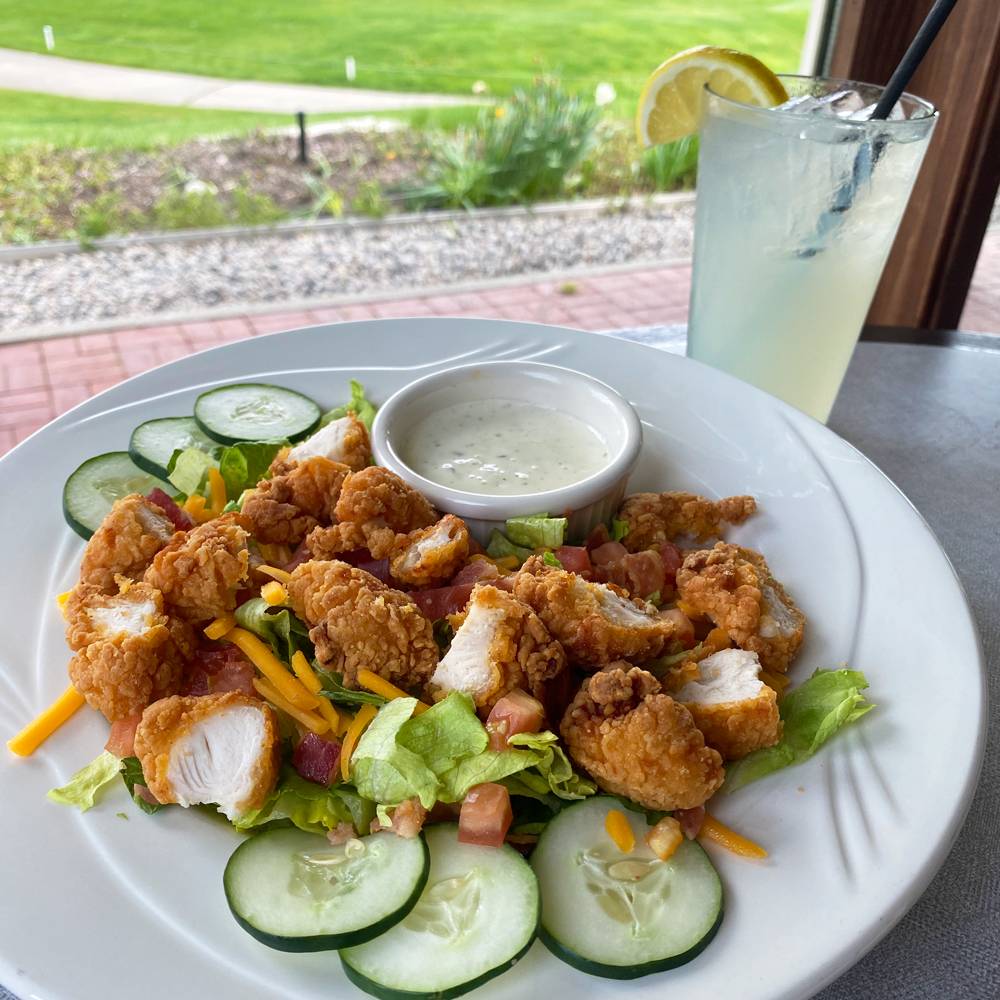 Crispy chicken salad on a plate with a glass of lemonade